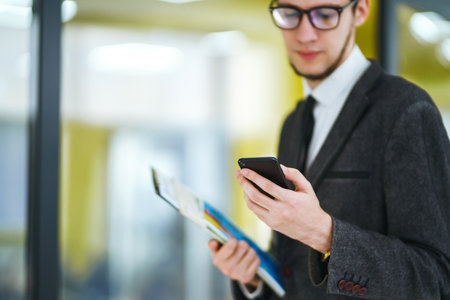 Man's hands using mobile phone standing in the modern office. businessman holding telephone in hand.の写真素材