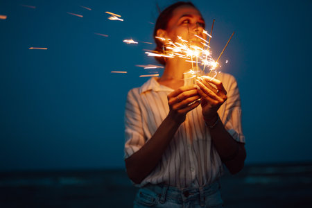 Glowing sparkles in hands. Women with Christmas sparklers on nature and twill light sky background.