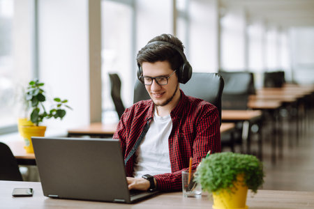 Creative man looking at screen typing message with smartphone. Young man relaxing using laptop.