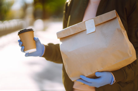 courier in medical mask and gloves delivers on a scooter a bag of food in quarantine city.の写真素材