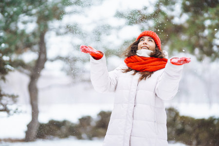 Winter smiling woman in red hat posing in a snowy park. cold weather. Winter fashion, holidays.の写真素材
