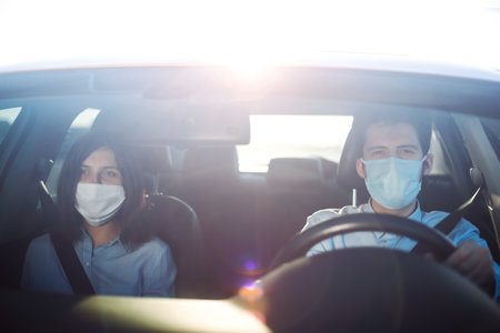 Young man and woman driving in a car during coronavirus quarantine in medical masks. safe taxi