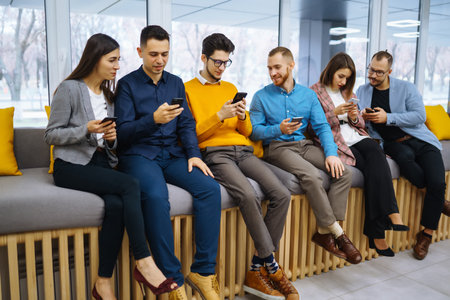 Group of young people using mobile phone. Business colegios sitting side by side in a modern office.