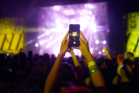 Hand with a phone records live music festival. People taking photographs with smart phone during concert.の写真素材