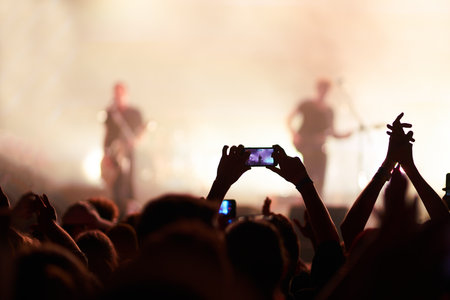 Hand with a phone records live music festival. People taking photographs with smart phone during concert.の写真素材