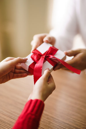 Man gives to his woman a gift box with red ribbon. Hands of man gives surprise gift box for girl.の写真素材