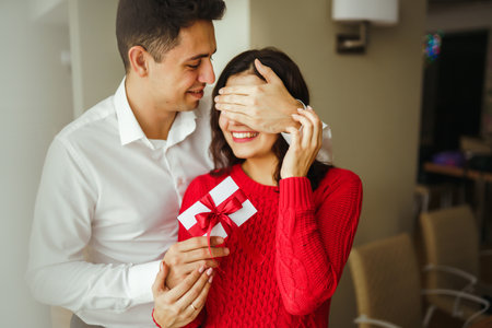 Young man gives his beloved a present and closes her eyes with a hand. Valentine's Day. Women's Day.の写真素材