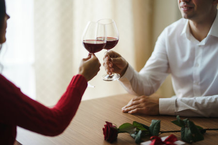 Couple click glasses with red wine. Lovers give each other gifts. Lovely romantic dinner.の写真素材