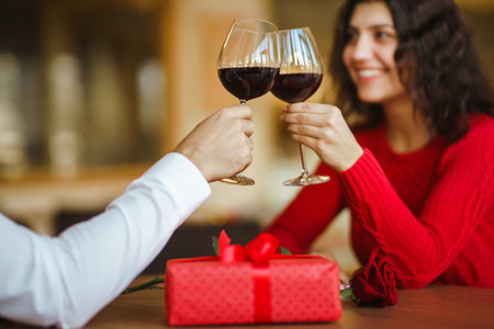 Couple click glasses with red wine. Lovers give each other gifts. Lovely romantic dinner.の写真素材