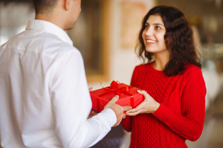 Man gives to his woman a gift box with red ribbon. Valentine's Day, holiday and surprise concept.の写真素材