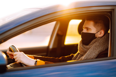 Young man in protective sterile medical mask driving car in quarantine city.の写真素材