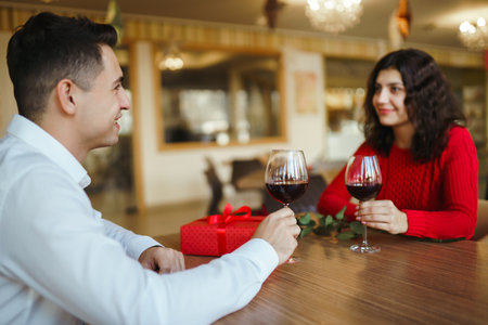 Couple click glasses with red wine. Lovers give each other gifts. Lovely romantic dinner.の写真素材