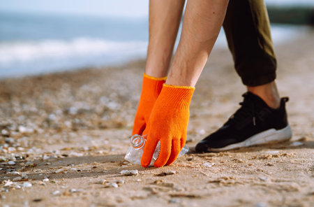 Trash on the beach. Men hand wearing protective gloves collects bottle plastic on sea beach.の写真素材