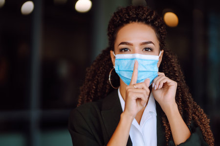Portrait of brunette woman in sterile medical mask on her face looking at camera outdoors close up.