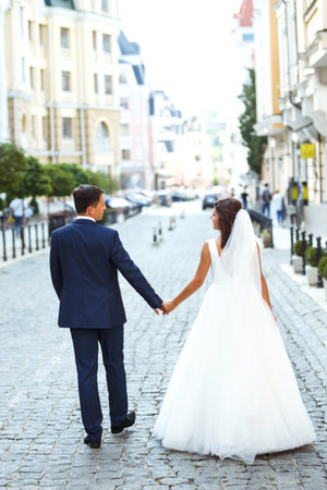 Gorgeous wedding couple walking in the city. Groom in stylish suit, bride in beautiful white dress.の写真素材