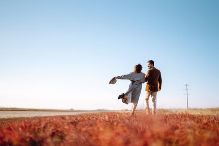 Stylish couple enjoying autumn weather in autumn field. Lovely couple walking in the field together.の写真素材