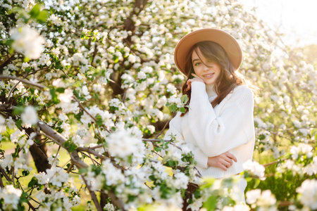 Smiling woman with hat posing in blooming spring park. The concept of relax, travel. fashion style.の写真素材