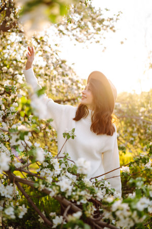 Smiling woman with hat posing in blooming spring park. The concept of relax, travel. fashion style.の写真素材