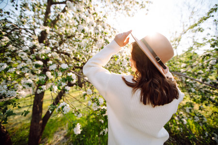 Portrait of Beautiful Woman In hat posing near flowering. Smiling woman enjoying the smell of flowers.の写真素材