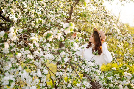 Smiling woman with hat posing in blooming spring park. The concept of relax, travel. fashion style.の写真素材