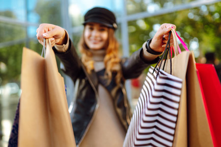 Smiling woman with shopping bags using her phone. Young woman after shopping on the city street.の写真素材