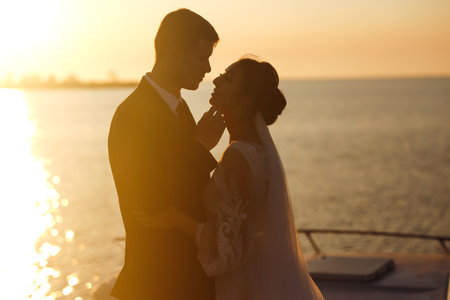 Beautiful bride and stylish groom together on the bridge against the background of the boat at sunset.の写真素材