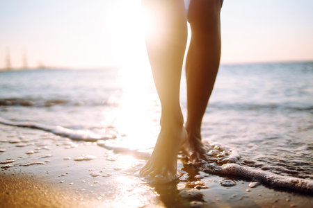 Close- up leg of young woman walking along wave of sea water and sand on the summer beach.の写真素材