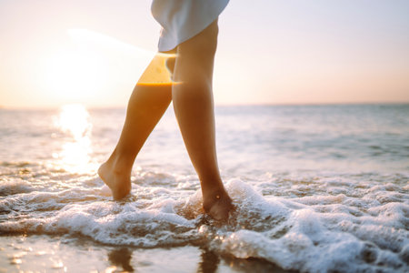 Close- up leg of young woman walking along wave of sea water and sand on the summer beach.の写真素材