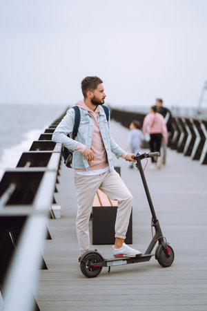 Modern Young man riding electric scooter on a pier near the sea. Ecological transportation concept.の写真素材