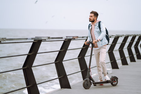 Modern Young man riding electric scooter on a pier near the sea. Ecological transportation concept.の写真素材