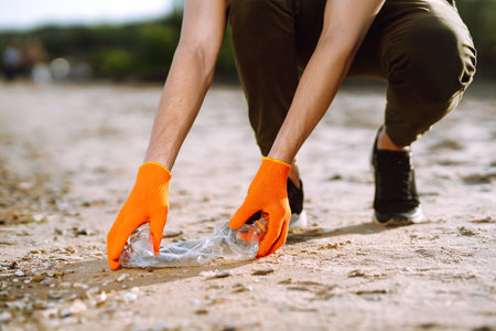 Trash on the beach. Men hand wearing protective gloves collects bottle plastic on sea beach.の写真素材