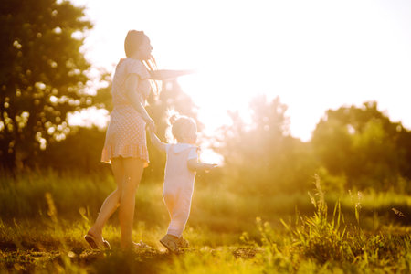 Mother and daughter playing together in summer park at sunset. happy mom with small child having funの写真素材