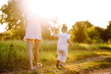 Mother and daughter playing together in summer park at sunset. happy mom with small child having funの写真素材