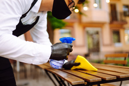 Disinfecting to prevent COVID-19. Waiter in protective face mask and gloves cleaning.の写真素材