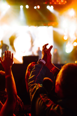 ?rowd with raised hands at music festival. Fans enjoying rock concert with light show clapping hands