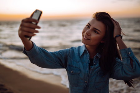 Beautiful girl takes a selfie on the beach at sunset. The concept of relax, travel and summer vacation.の写真素材