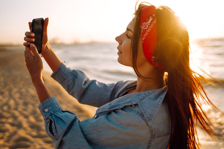 Beautiful girl takes a selfie on the beach at sunset. The concept of relax, travel and summer vacation.の写真素材