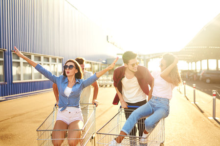 Group of happy young people having fun on shopping trolleys. Multiethnic young people racing on shopping cart.の写真素材