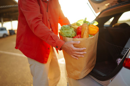 Healthy vegan vegetarian food in a paper bag in the male hands. Man with shopping bag near the car.