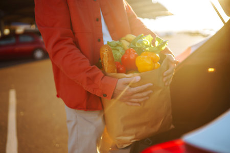 Healthy vegan vegetarian food in a paper bag in the male hands. Man with shopping bag near the car.
