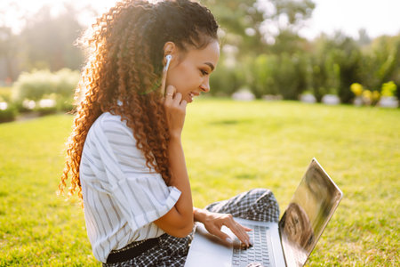 Young woman freelancer sitting on green grass with laptop. education online.の写真素材