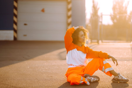 Young African American woman - dancer dancing in the street at sunset. Stylish woman with curly hair in an orange suit showing some moves.の写真素材