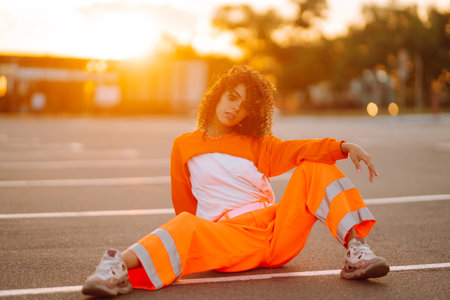Young African American woman - dancer dancing in the street at sunset. Stylish woman with curly hair in an orange suit showing some moves.の写真素材