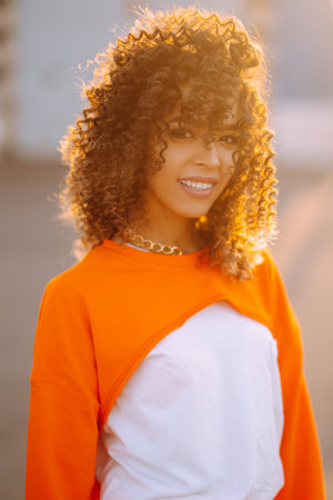 Stylish woman - dancer dancing in the street at sunset. Beautiful African American woman with curly hair in an orange suit.の写真素材