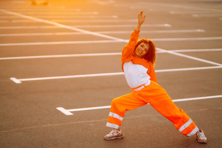 Young African American woman - dancer dancing in the street at sunset. Stylish woman with curly hair in an orange suit showing some moves.の写真素材
