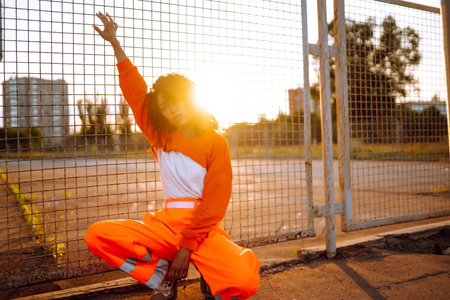 Young African American woman - dancer dancing in the street at sunset. Stylish woman with curly hair in an orange suit showing some moves.の写真素材