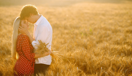 Young happy couple hugging on a wheat field, on the sunset. enjoying time together.の写真素材