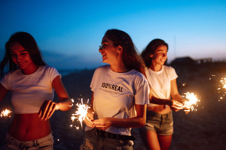 Group of friends at night on the beach with sparklers. Young friends enjoying on beach holiday.の写真素材