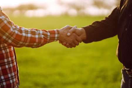 Handshake two farmer on the background of a wheat field at sunset. The concept of the agricultural.の写真素材