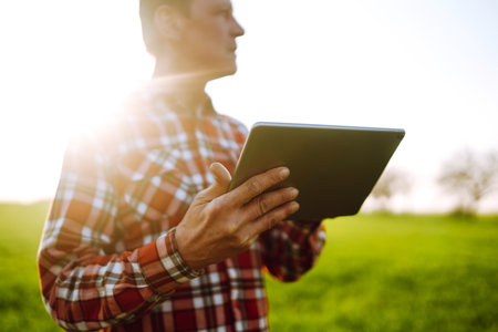 Farmer on a green wheat field with a tablet in his hands. Farmer checking his crops on an...